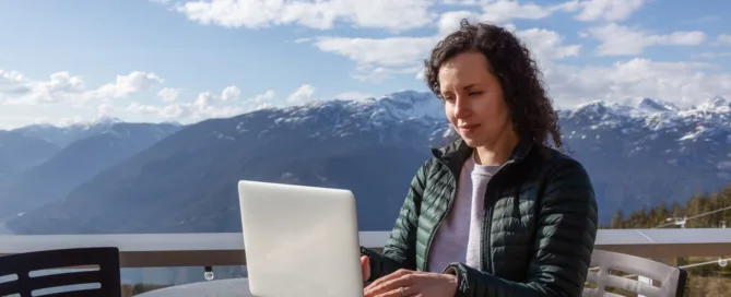 Woman digital nomad works on her laptop by the mountains in Canada